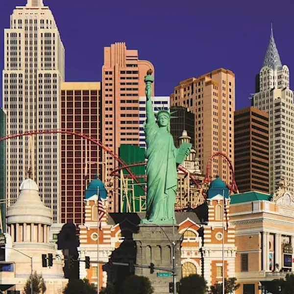 A replica of the Statue of Liberty in front of a cityscape with tall buildings and a roller coaster in Las Vegas.