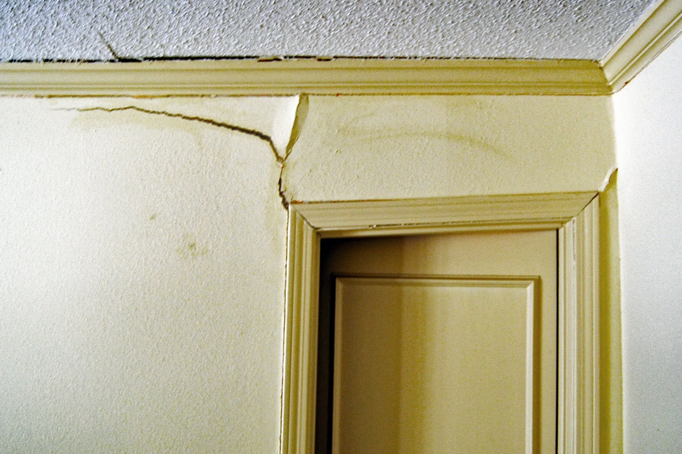 Indications of significant foundation damage inside a slab foundation home including heavily leaning door header, large separated crack in the sheetrock wall, and a door that doesn't close found during a home inspection..
