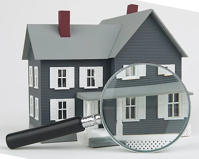 Model of a dark blue house with white window shutters, a gray roof, a chimney, and a front porch, with a magnifying glass examining part of the house.