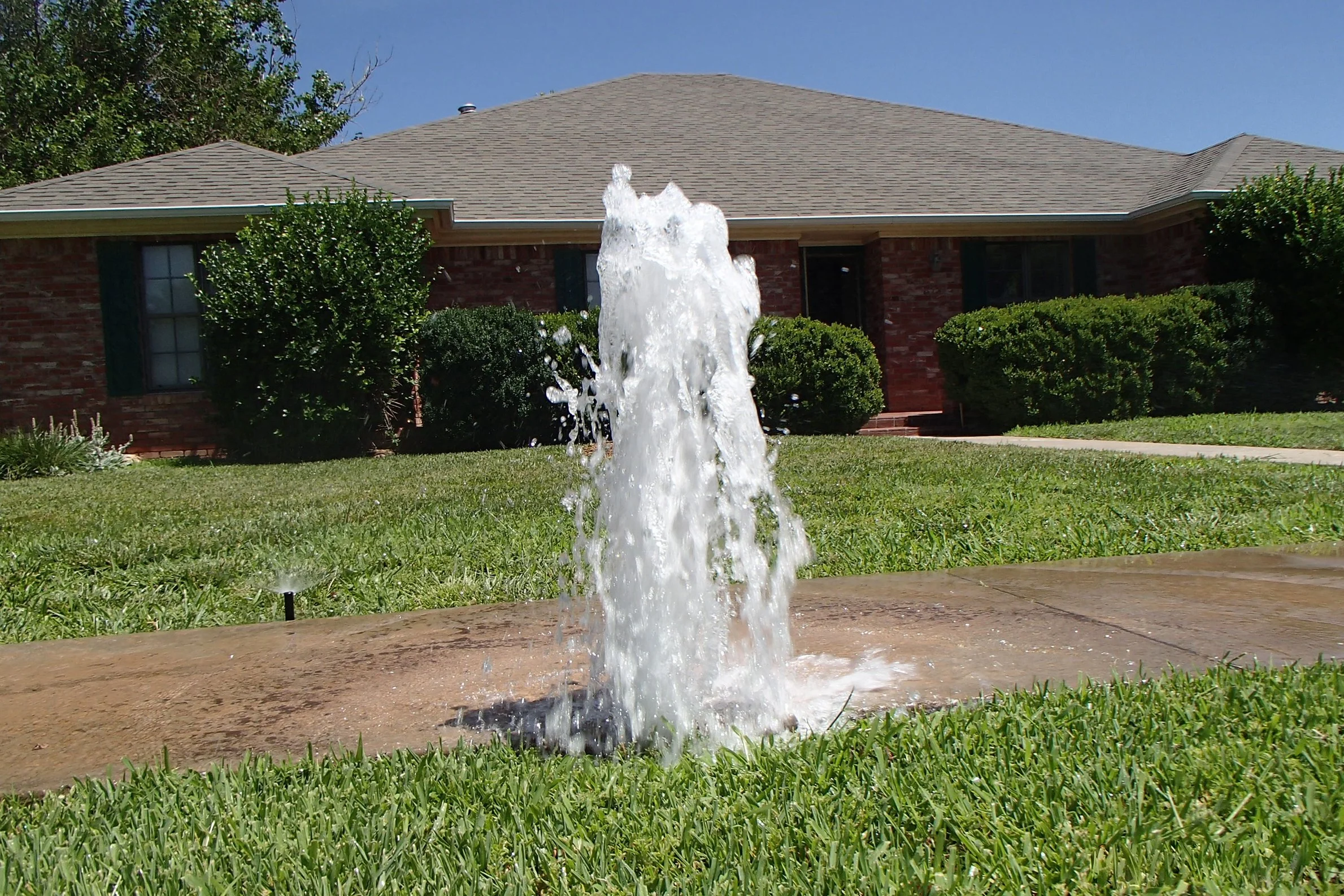 Broken and missing sprinkler system spray head resulting in a large amount of water spraying from the ground found during a home inspection.