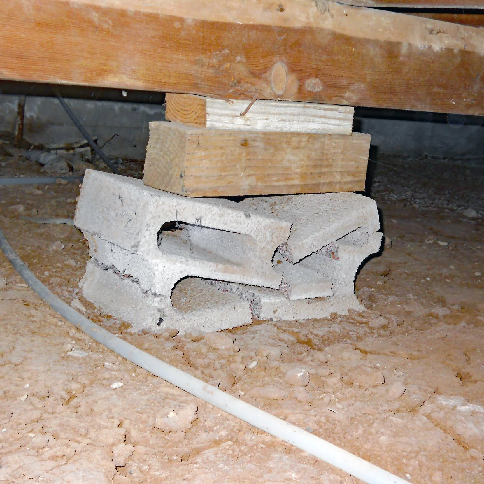 A crushed improperly installed concrete masonry unit foundation pier in a crawlspace of a pier and beam home found during a home inspection.