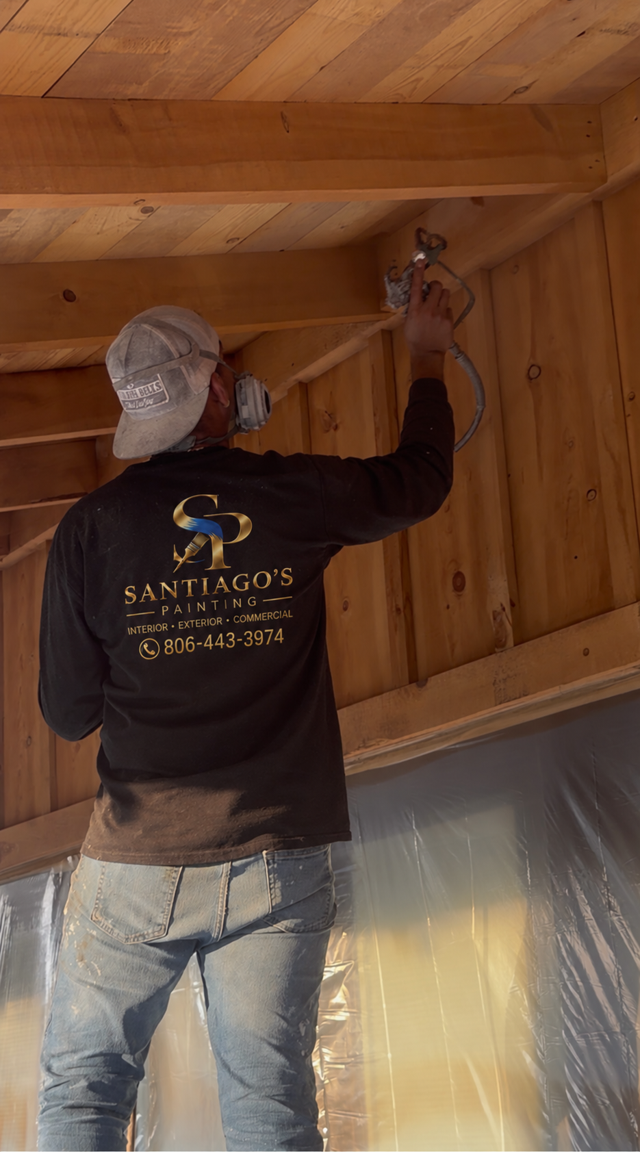A worker wearing a Santiago's Painting uniform and mask is spray painting a wooden ceiling.