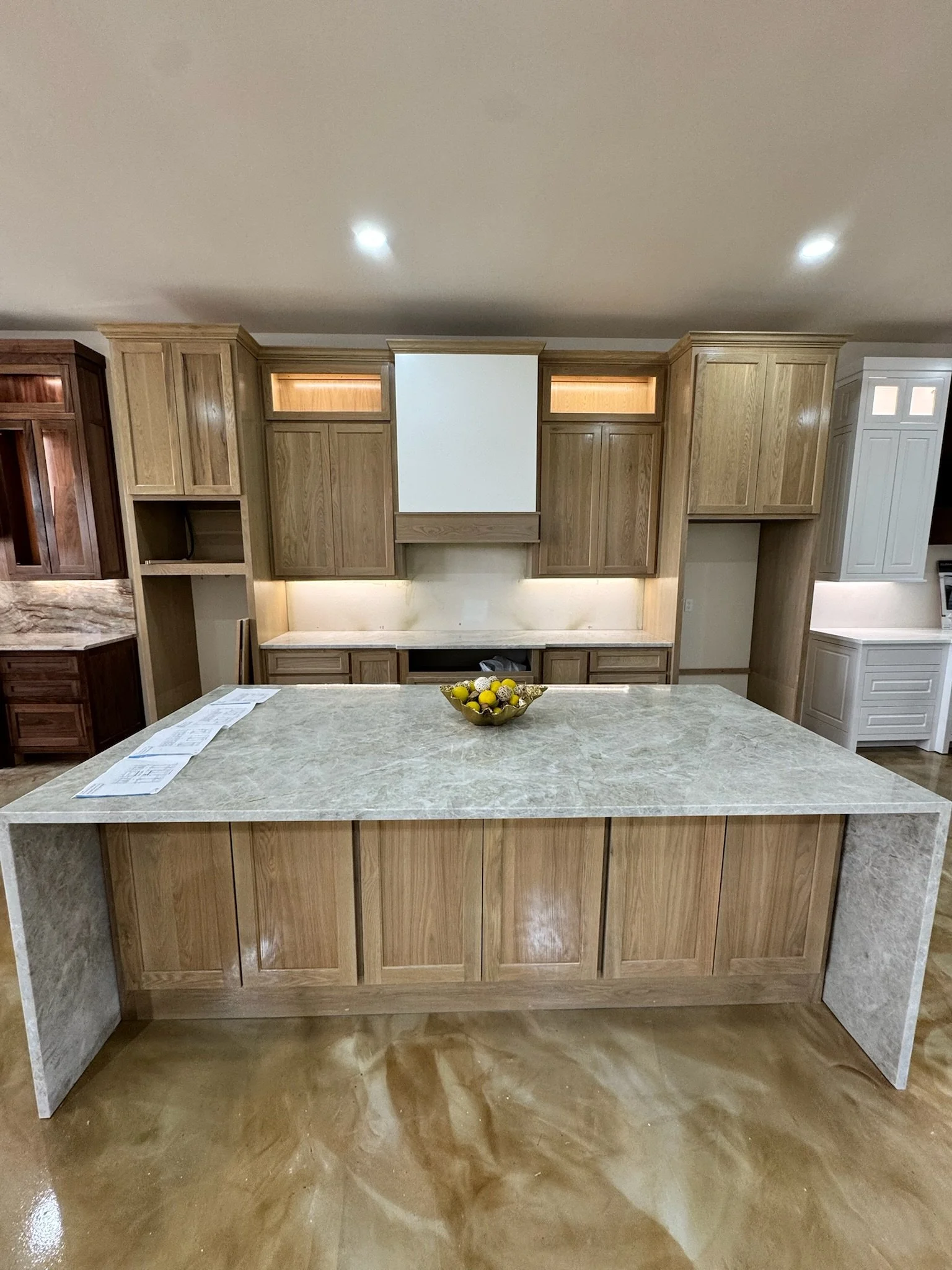 Kitchen with wooden cabinets, a large island with a marble countertop, and a bowl of lemons in the center.