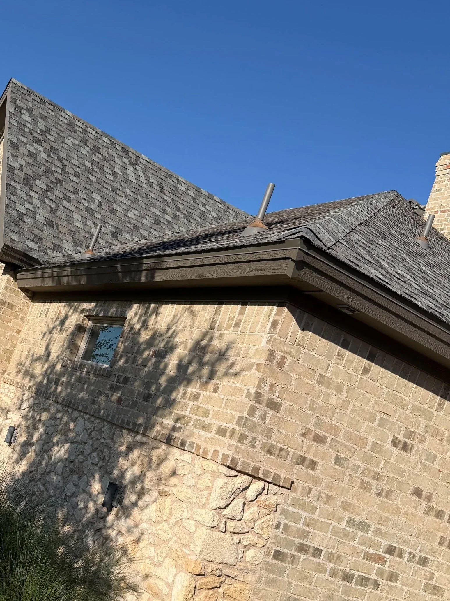Close-up view of a brick house with a roof, chimney, and metal vents under a clear blue sky.