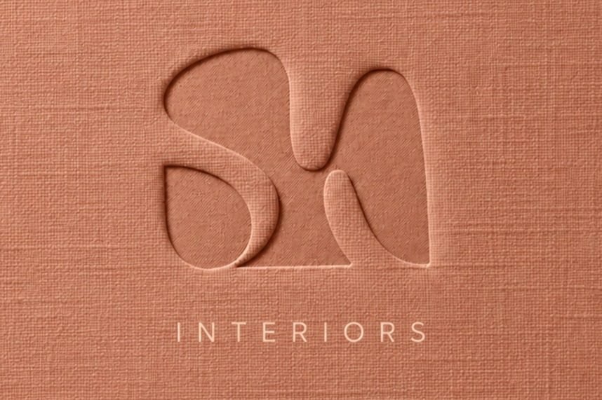 Close-up view of a textured, tan-colored surface with cut-out shapes forming the initials 'S' and 'N', and the word 'INTERIORS' below.