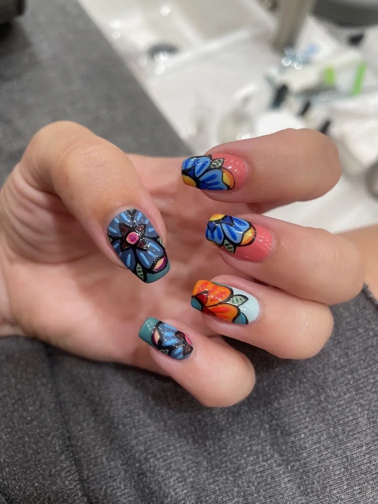Colorful floral nail art with blue, black, and pink designs on each fingernail.