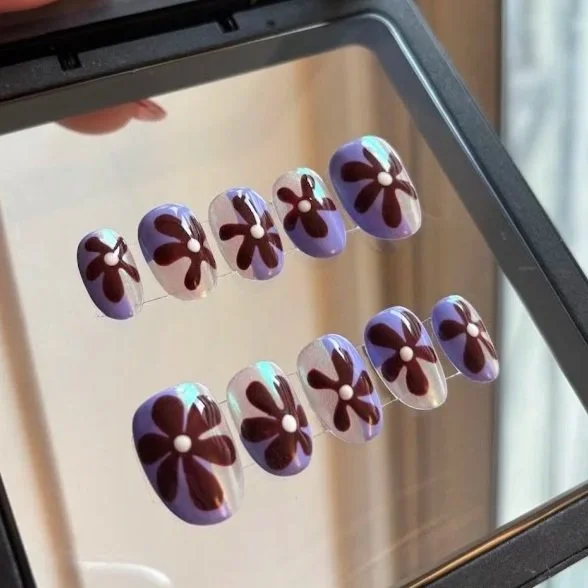 Nail art display with purple base color and white flowers on artificial nails.
