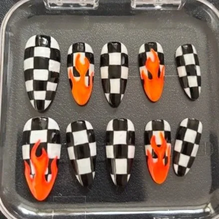 Five false nails with black and white checkered pattern and three nails with bright orange flame design.