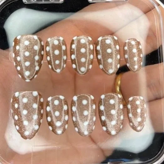 Set of ten cheetah print nails with white spots on a brown background, displayed on a hand.