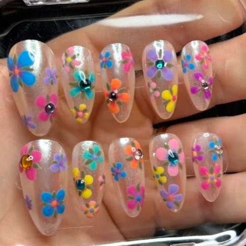 Nail art with colorful 3D floral designs and rhinestone accents on a clear nail base.