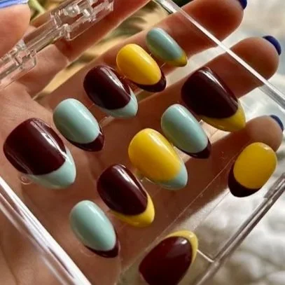 Close-up of multicolored gel nails in a clear plastic box, featuring yellow, light blue, and dark red shades.