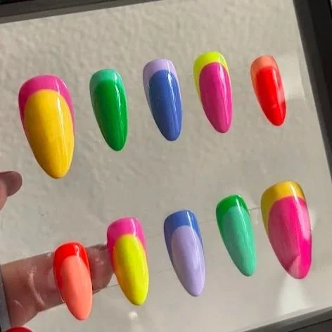 Colorful artificial nails with various bright colors and designs displayed on a transparent stand.