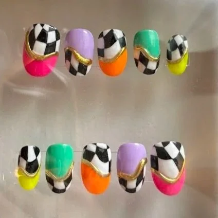 Colorful fake nails with black and white checkered patterns and gold accents.