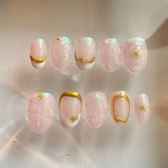 Set of artificial nails with pink marbled design, gold accents, and star-shaped embellishments.