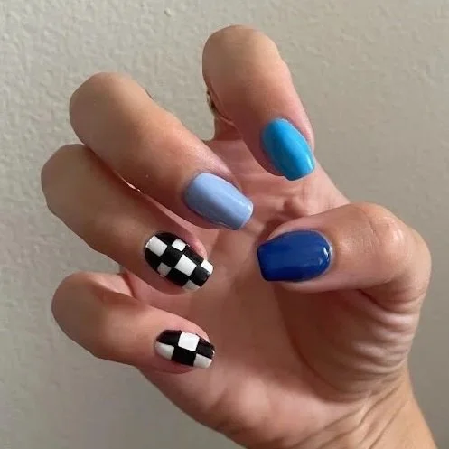 A hand with five fingernails painted in various shades of blue and black-and-white checkerboard patterns.