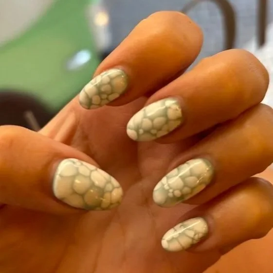 Hand showing nails with bubblegum pink color, decorated with greenish yellow and white bubble patterns.