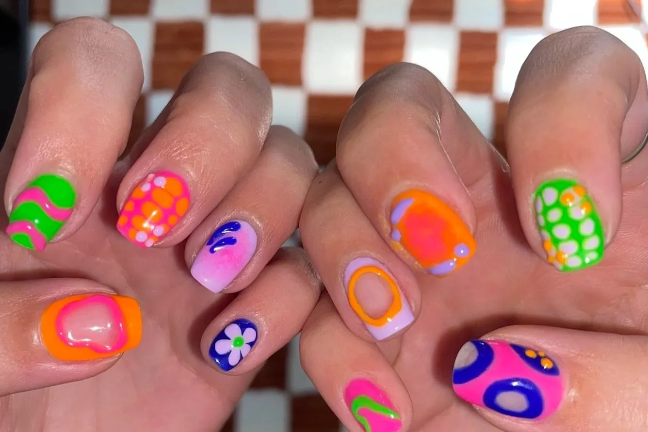 Colorful, neon nail art with various patterns including stripes, dots, circles, and floral designs on fingernails.