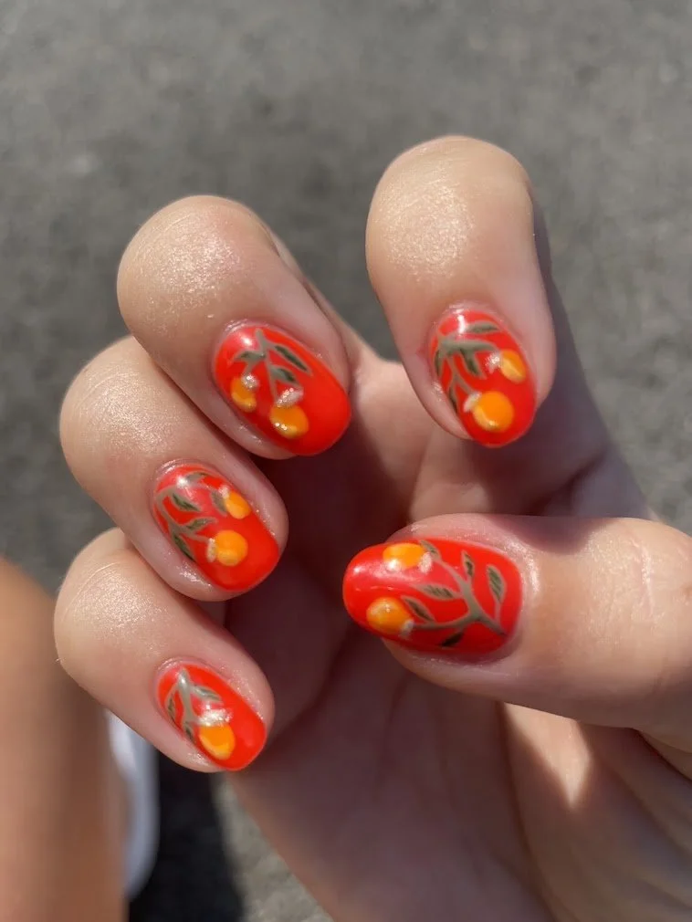 Close-up of a hand with colorful floral nail art featuring orange and yellow flowers on a red background.
