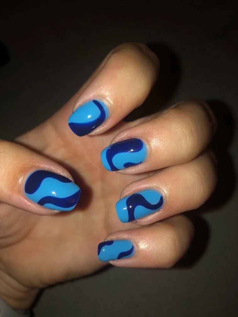 Hand with nails painted in blue with wavy dark blue patterns.