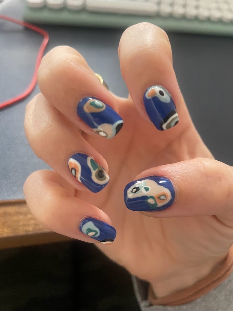 Person's hand showing nails painted with a colorful abstract pattern on a blue background.