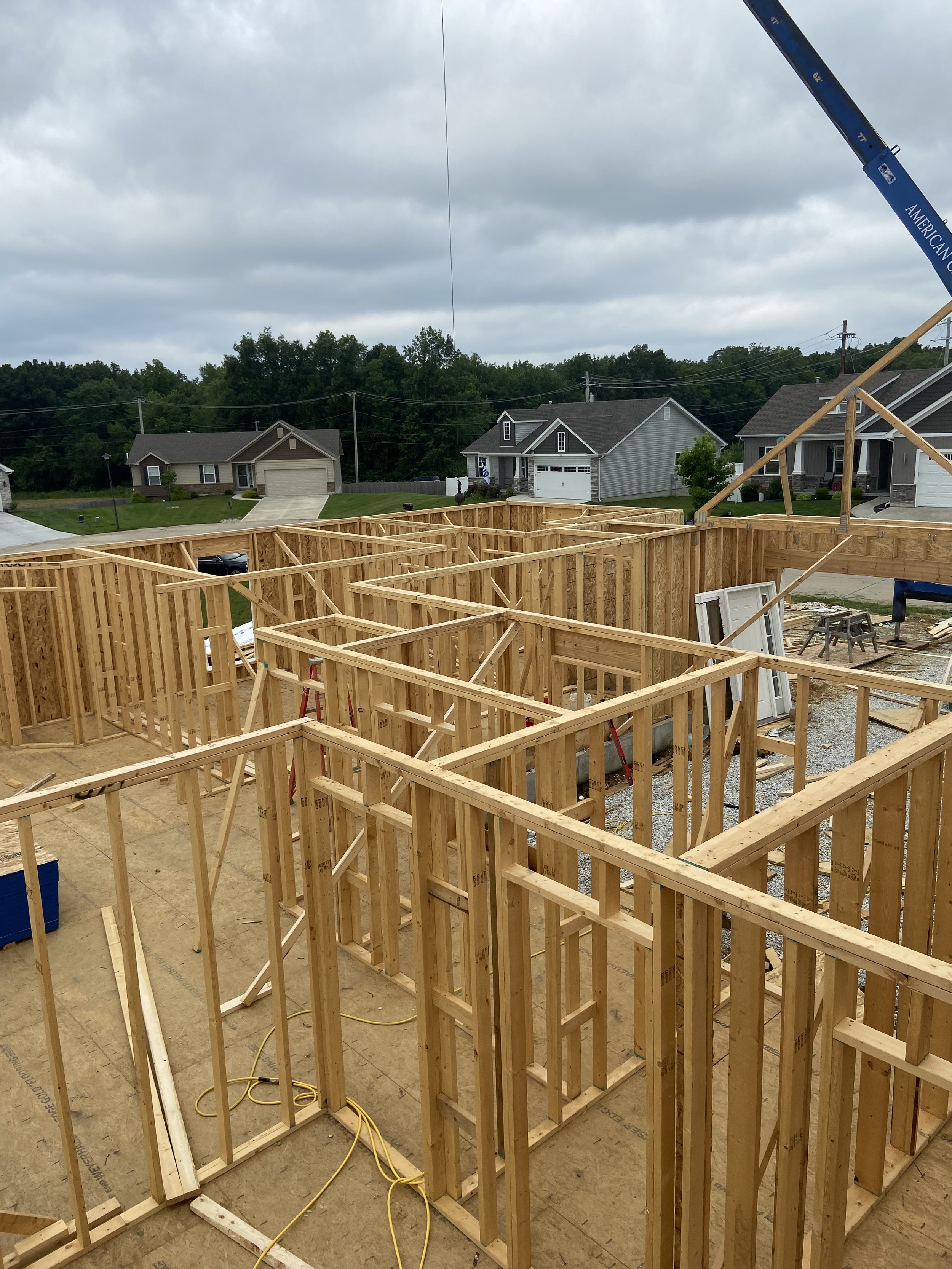 Wooden framework of a house under construction with neighboring houses and overcast sky in the background.