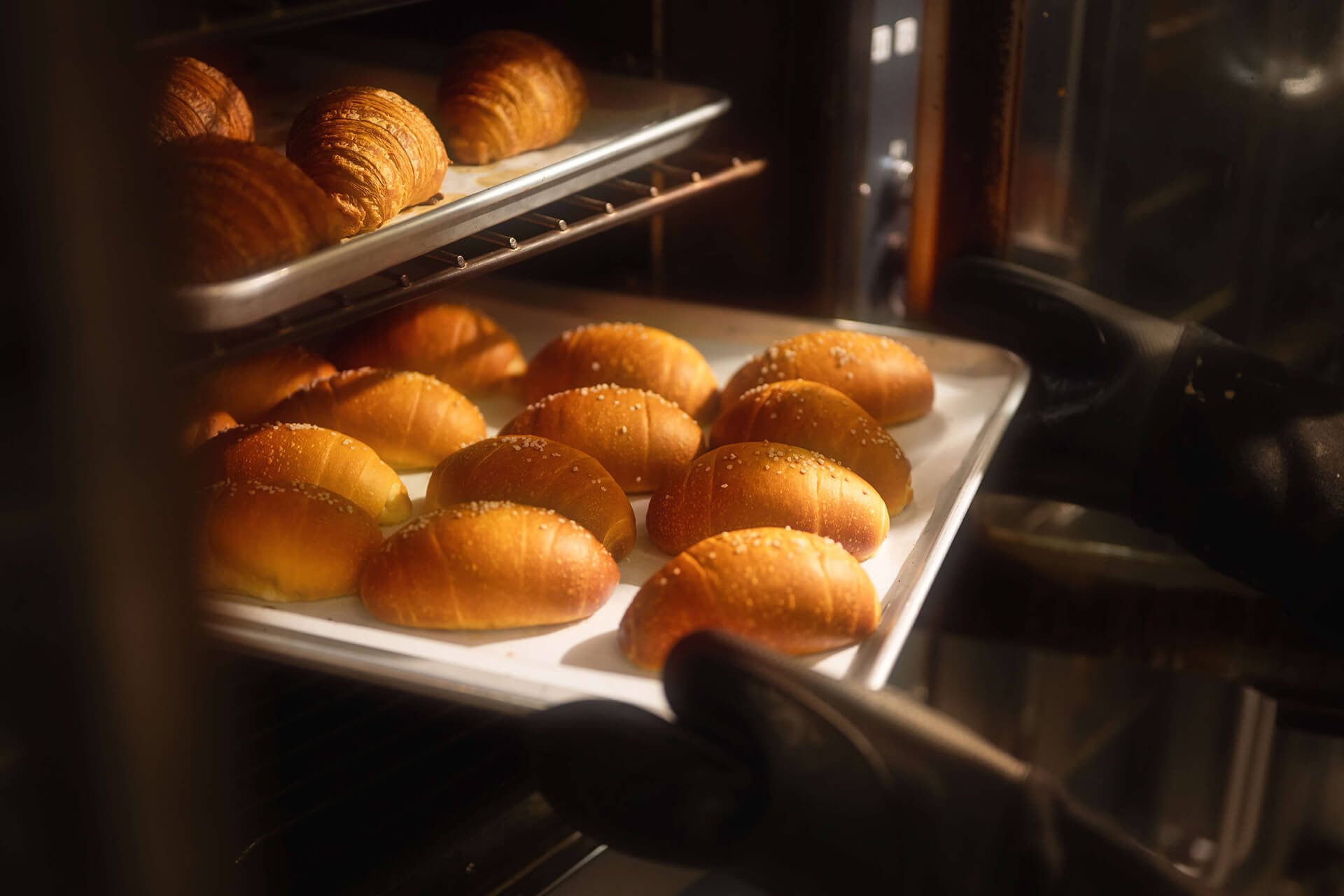 Croissants and bread rolls baking in an oven.