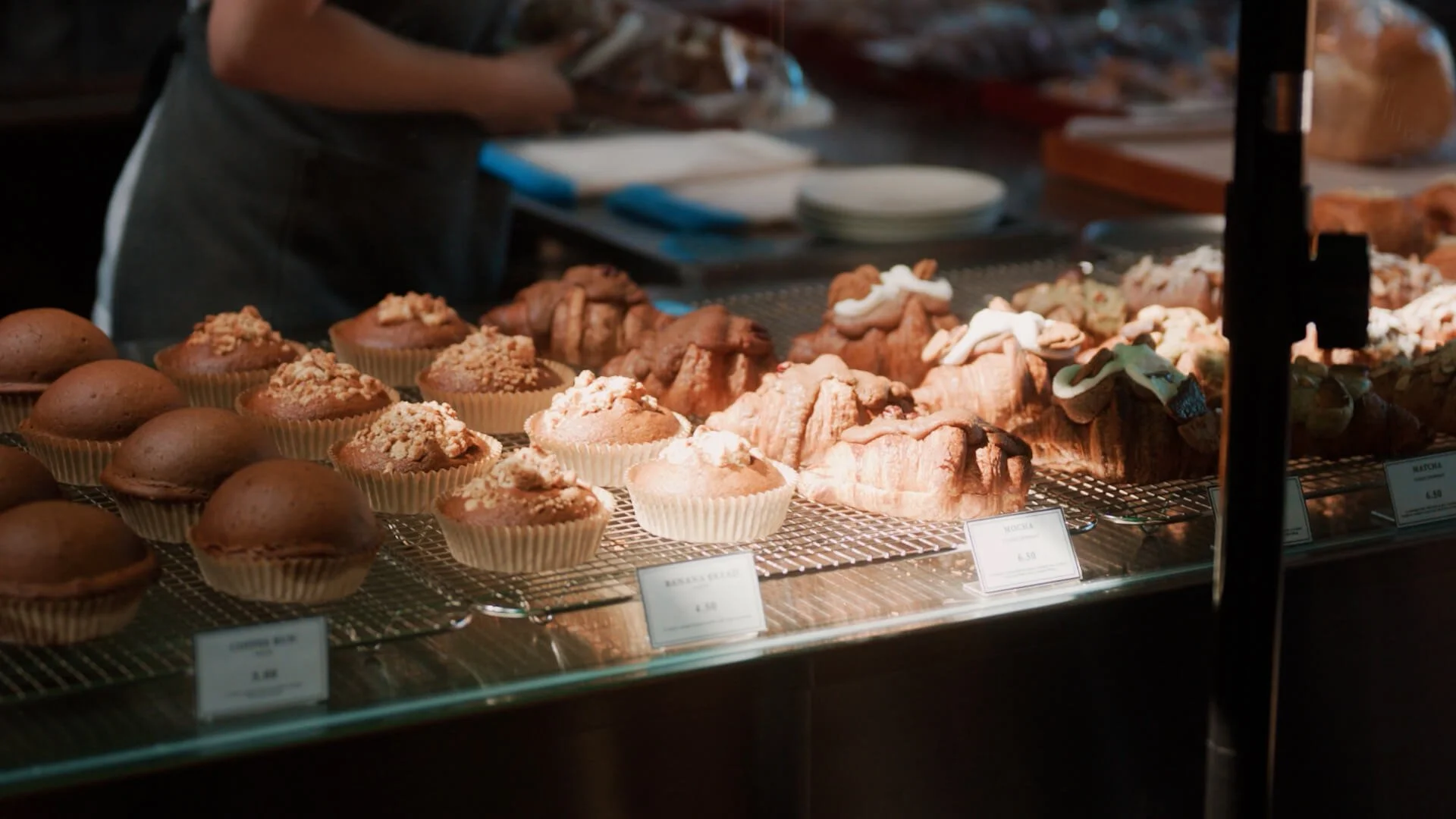 Display case with muffins topped with crumbs and pastries in a bakery.