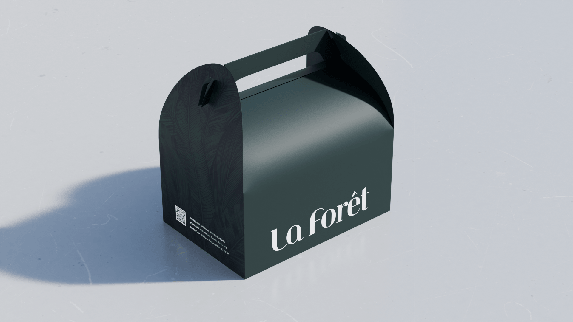 A black paper bag with the text "la forêt" printed in white, featuring a handle on top, sitting on a white surface with shadows.