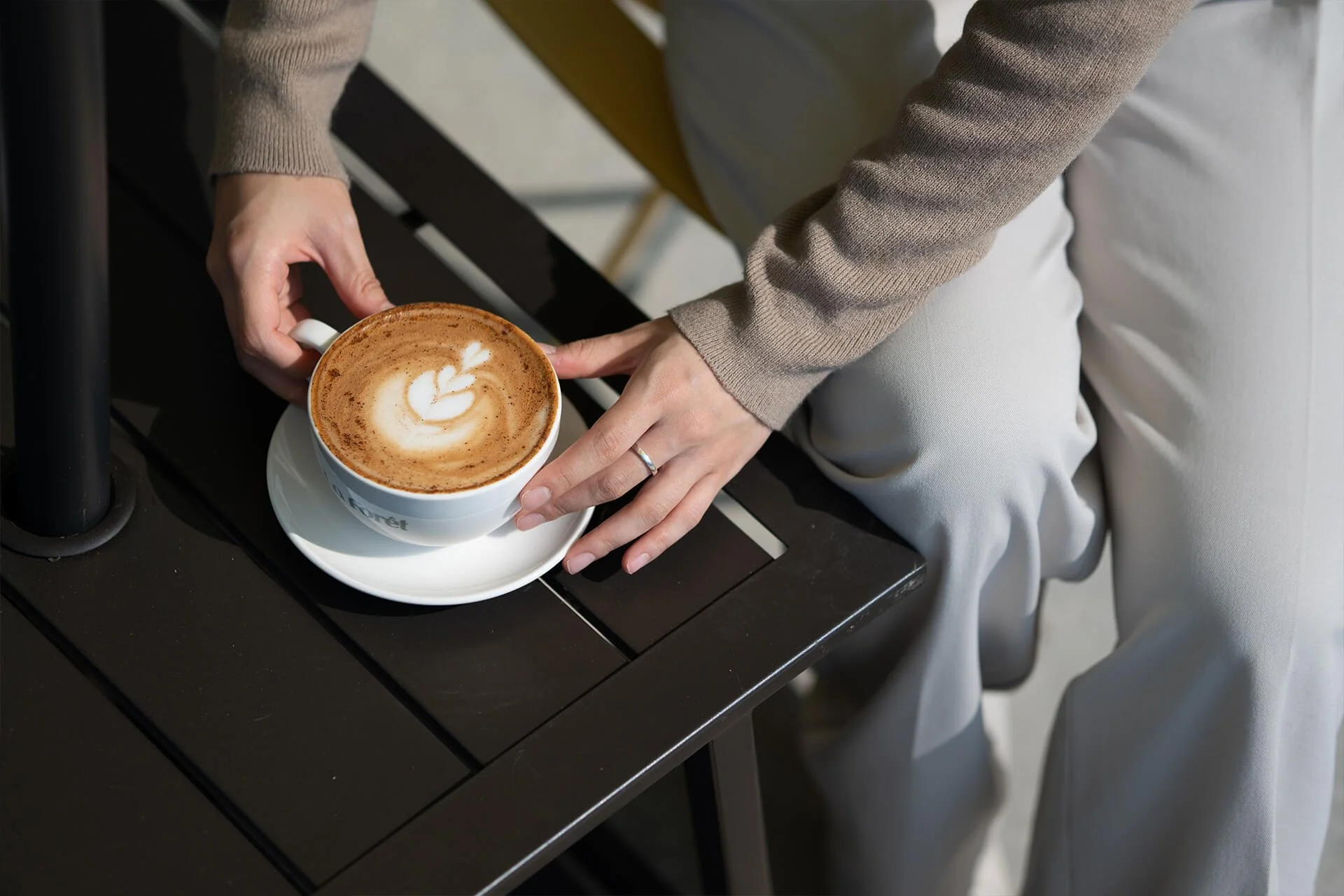 A person holding a cup of coffee with latte art, sitting at a dark table in a café.