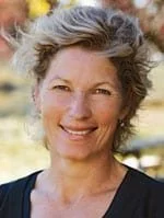 A smiling woman with short, curly, gray hair outdoors.
