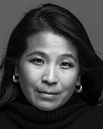 A black and white portrait of a woman with dark hair, wearing earrings and a dark top.