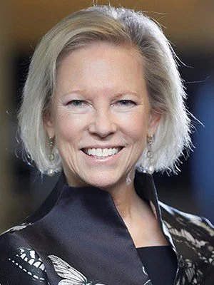 A smiling middle-aged woman with short blond hair, wearing a black blouse with a floral pattern.