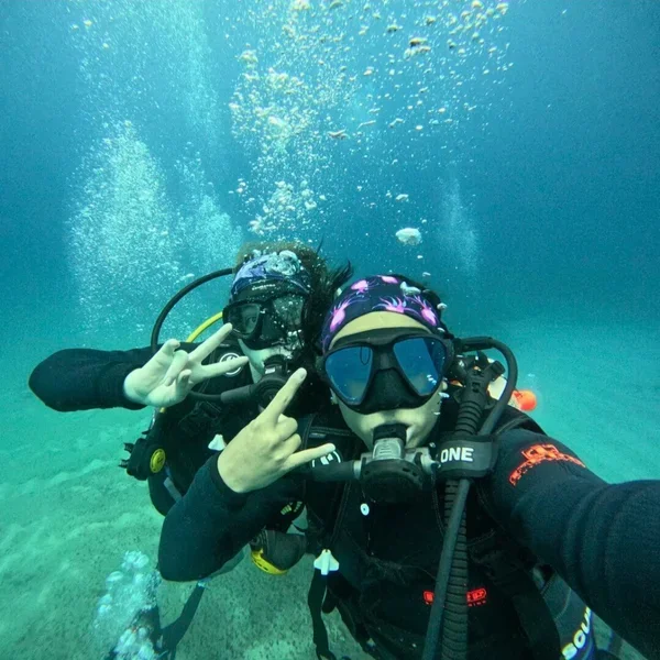 Two people scuba diving underwater, making peace signs with their hands.