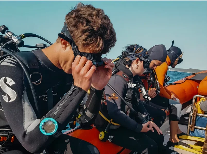 Four scuba divers on a boat preparing for a dive, with the ocean in the background.