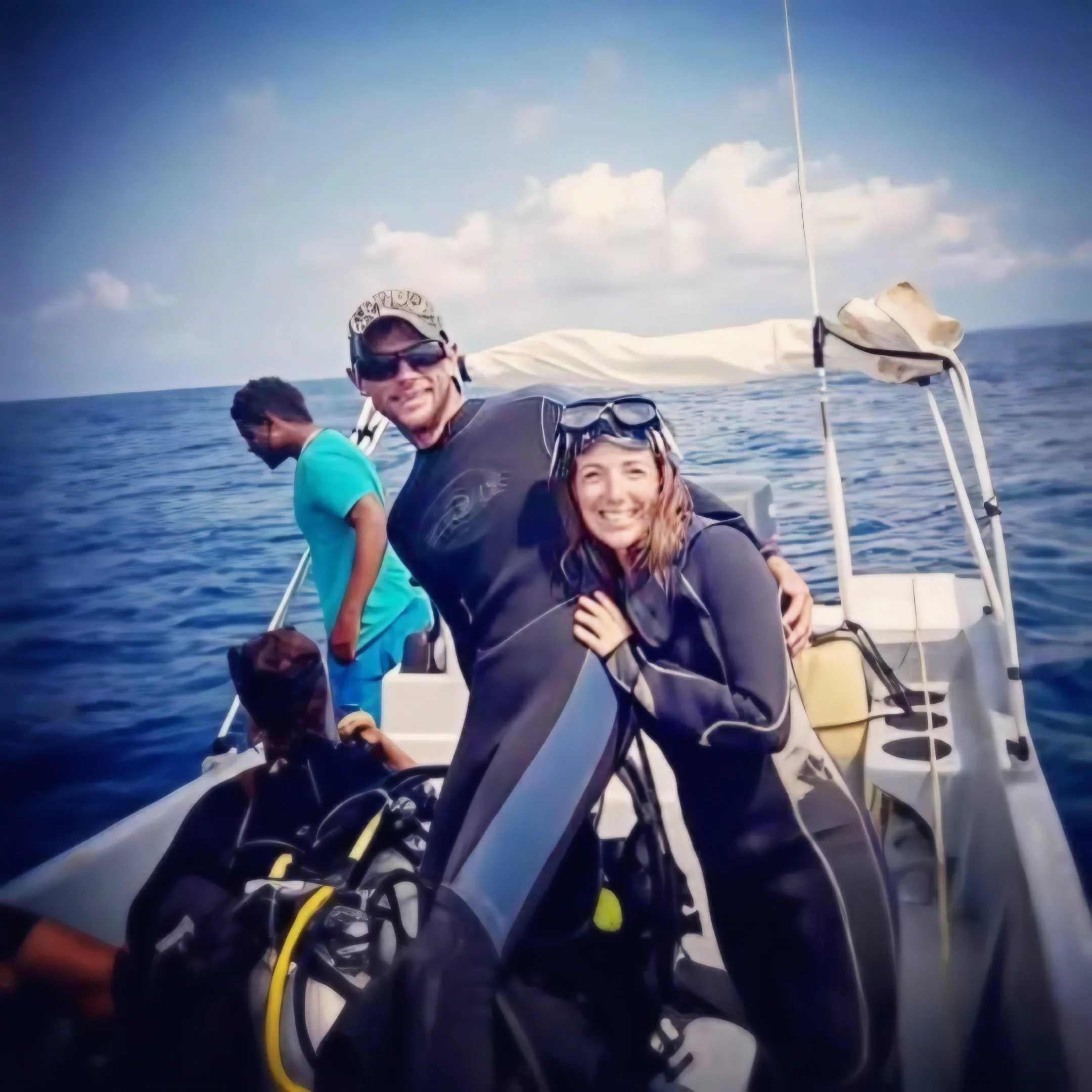 People smiling on a boat, with the ocean and sky in the background, and a flag or sail visible on the right side of the image.