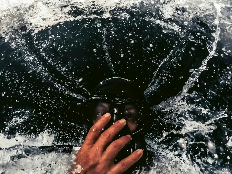 A person holding a mask in water, with water splashing around.