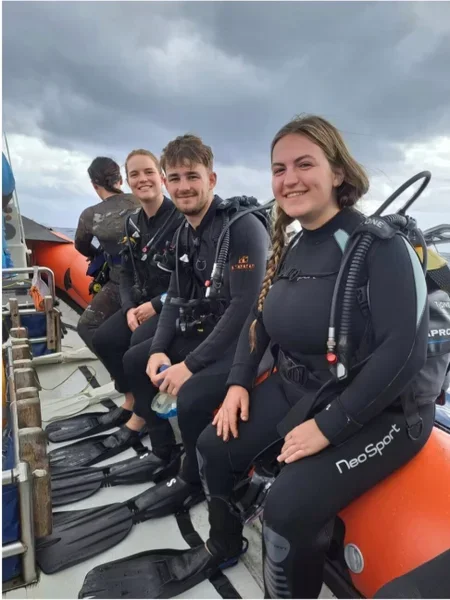 PADI Go Pro scuba diving students in full gear sitting aboard a boat with Savage Travel Co.