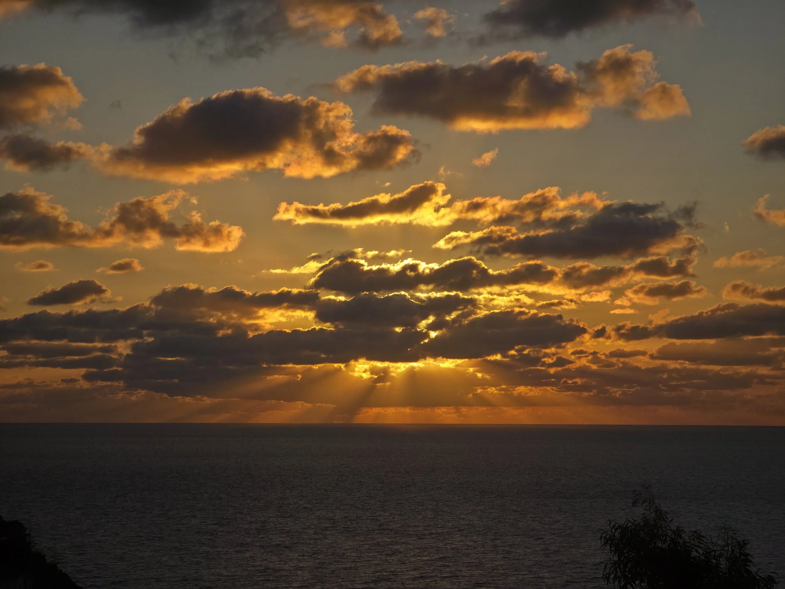 Sunset over the ocean with dark clouds and golden light illuminating the sky near the horizon.