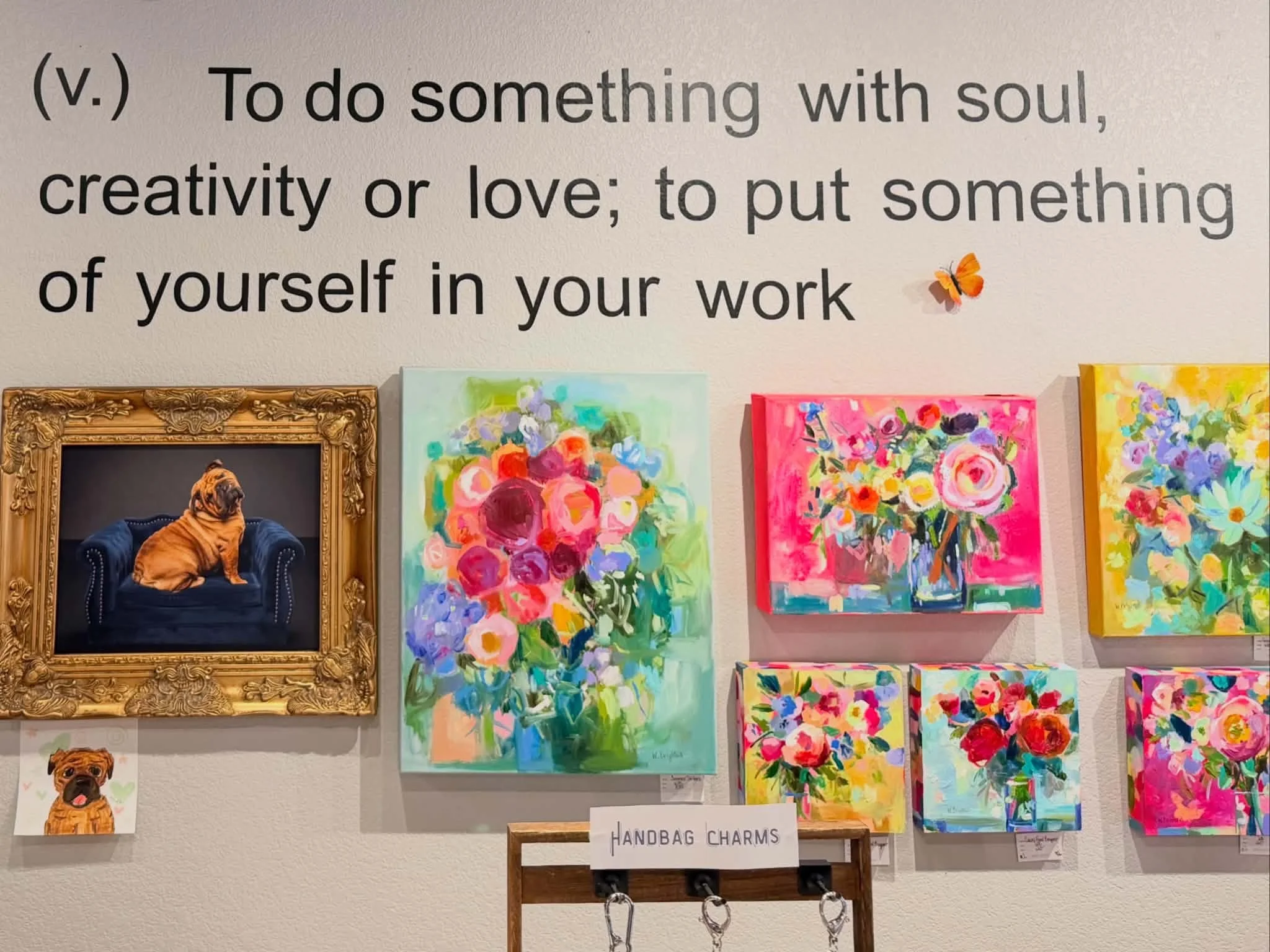 Wall display with quote about doing something with soul, creativity, or love, colorful floral paintings, and framed artwork of a dog.