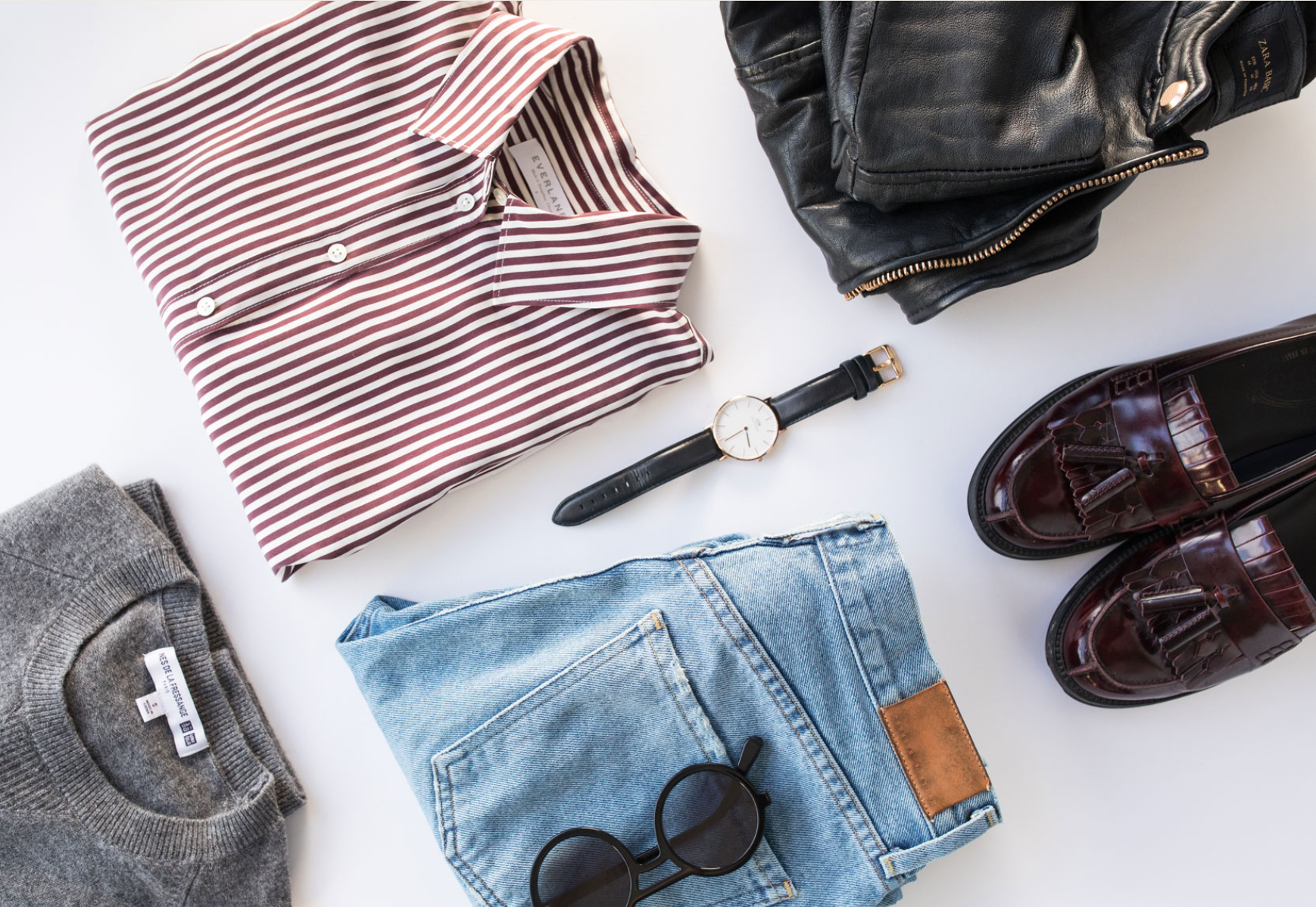 Collection of men's clothing and accessories including a striped shirt, gray sweater, pair of jeans, sunglasses, black watch, black leather purse, and burgundy leather shoes.