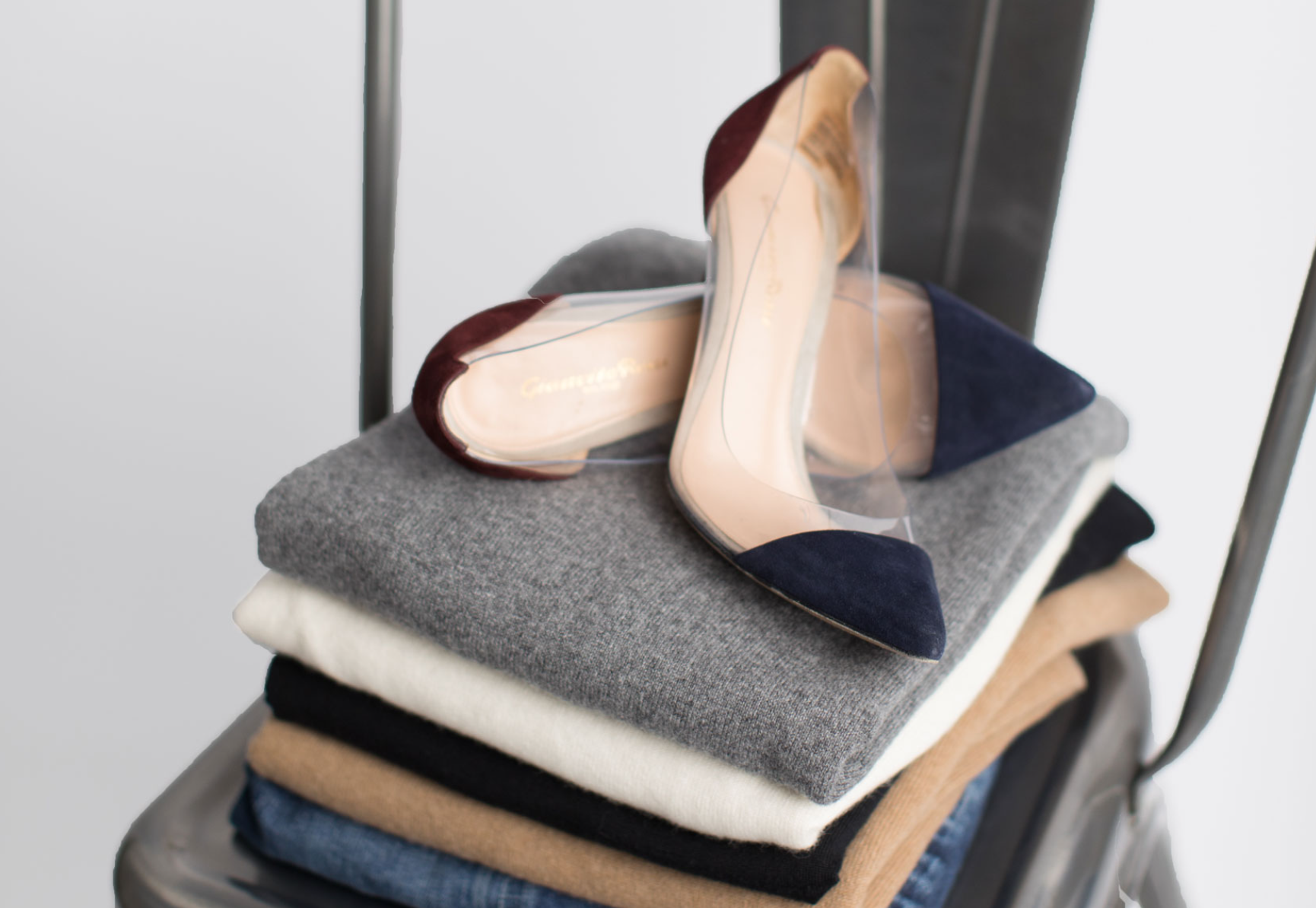 Stacked folded sweaters in various colors on a chair with a pair of high-heeled shoes resting on top.