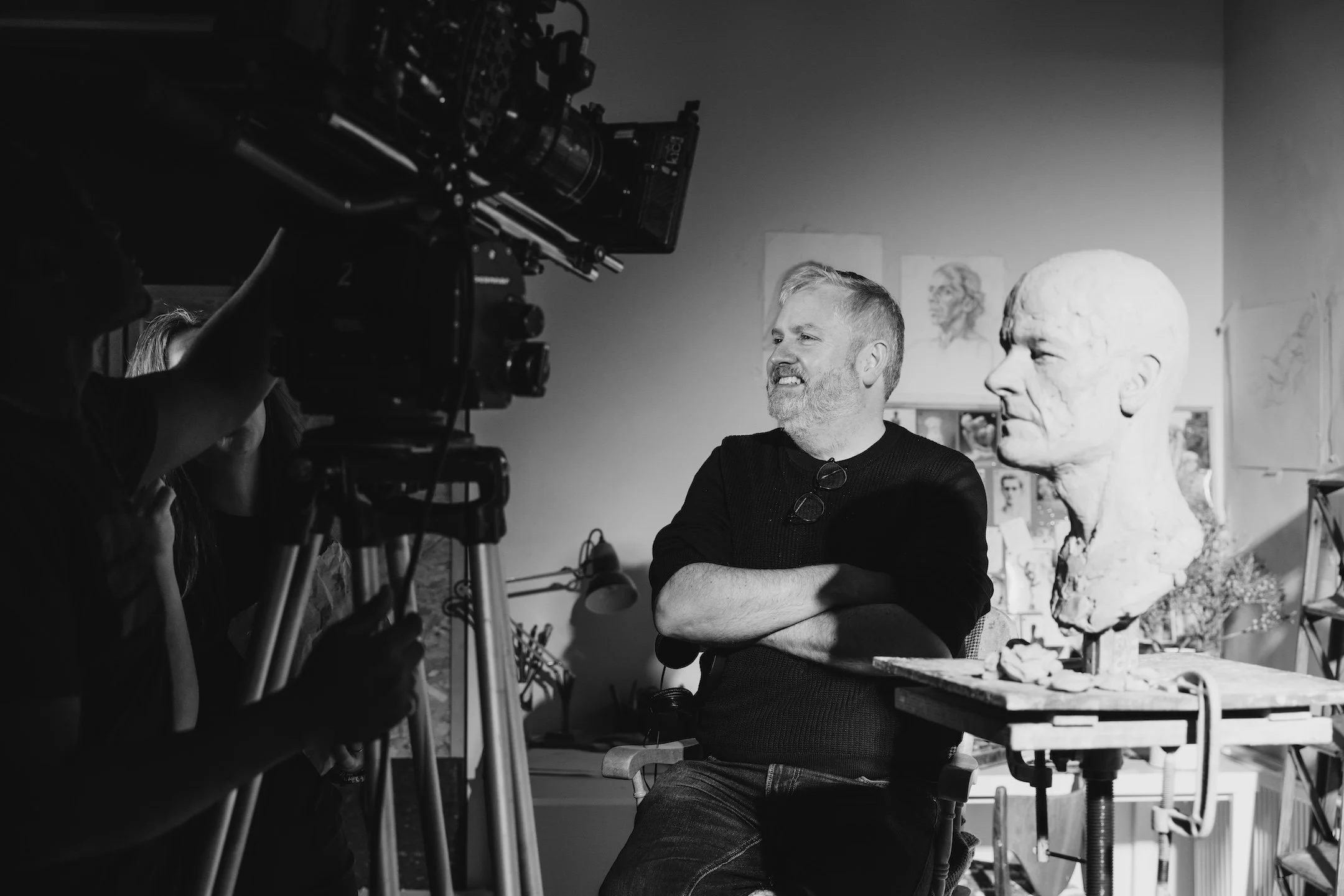 Benjamin Verrall on the set of Model Parent, standing beside a sculpted portrait while a camera crew sets up a shot.