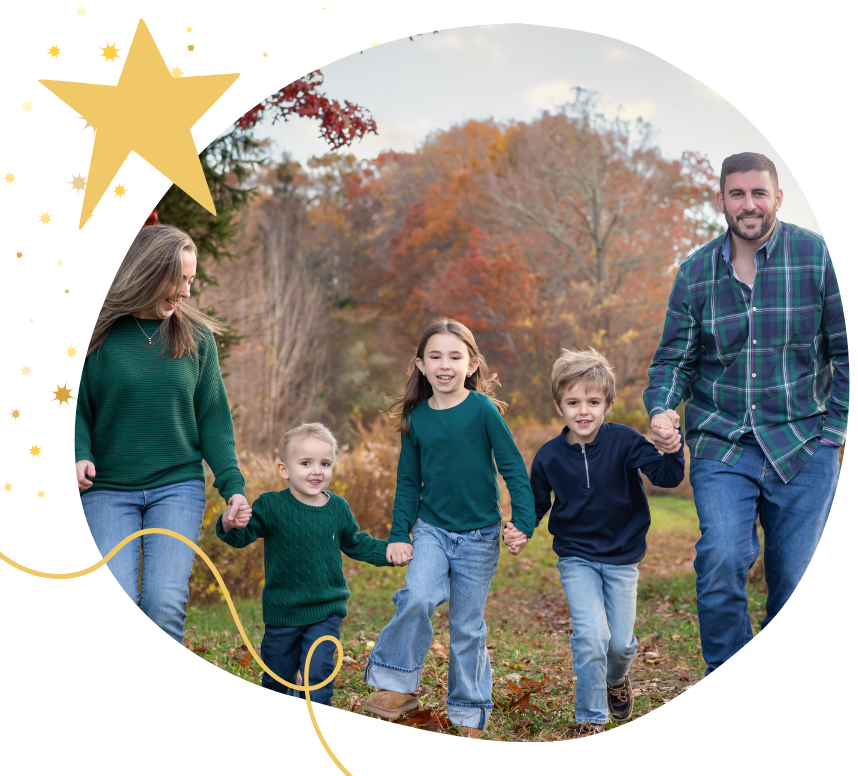 Family of five walking outdoors in fall, holding hands and smiling, with colorful autumn trees in background.