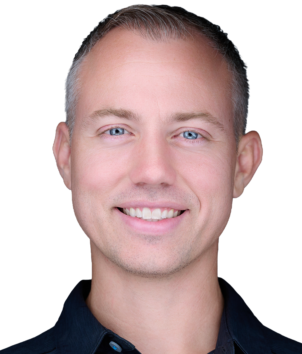 Close-up photo of a young man with short brown hair, blue eyes, smiling showing his teeth, wearing a dark collared shirt.