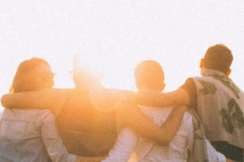 Group of five young friends sitting outdoors at sunset, showing camaraderie and friendship.