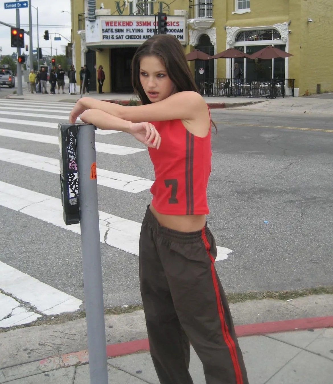 Young woman in athletic wear leaning on a parking meter at a crosswalk in an urban setting.