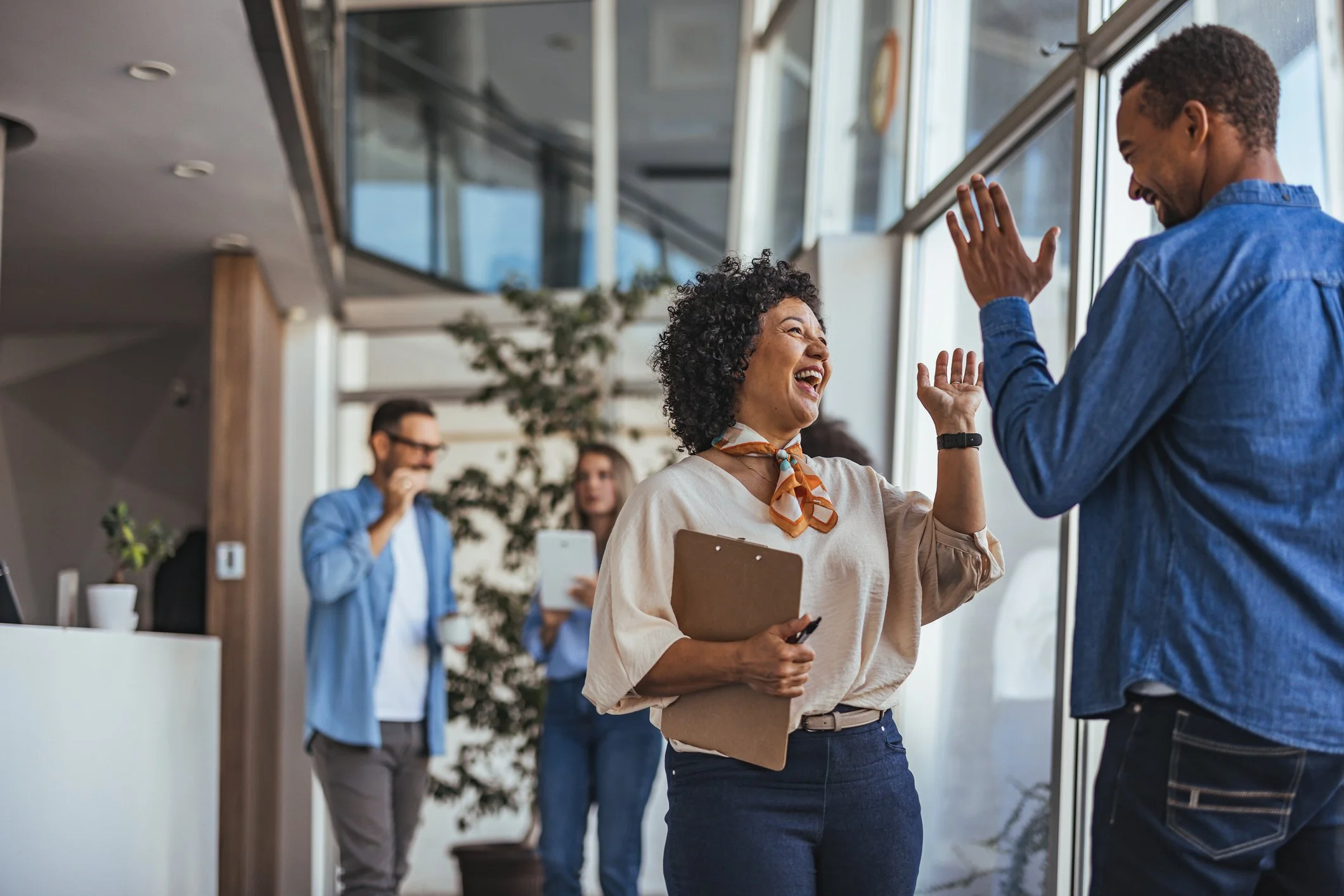 Two colleagues sharing a high-five in an office, with other coworkers in the background.