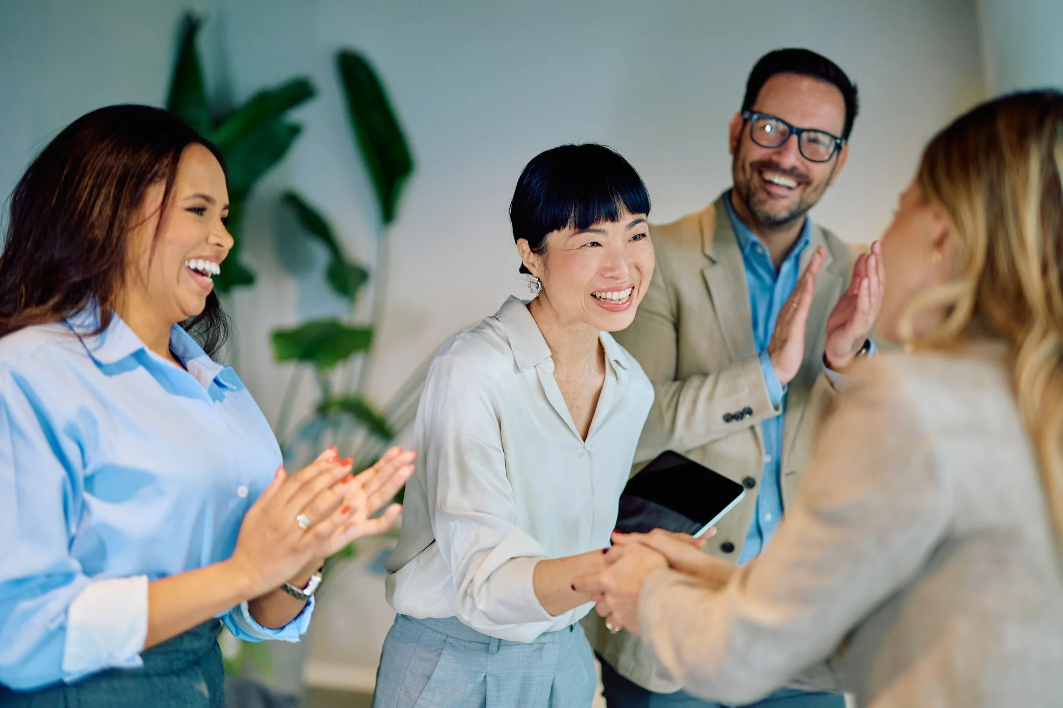 Group of diverse people at work, smiling, shaking hands, and engaging in conversation, in an office setting.