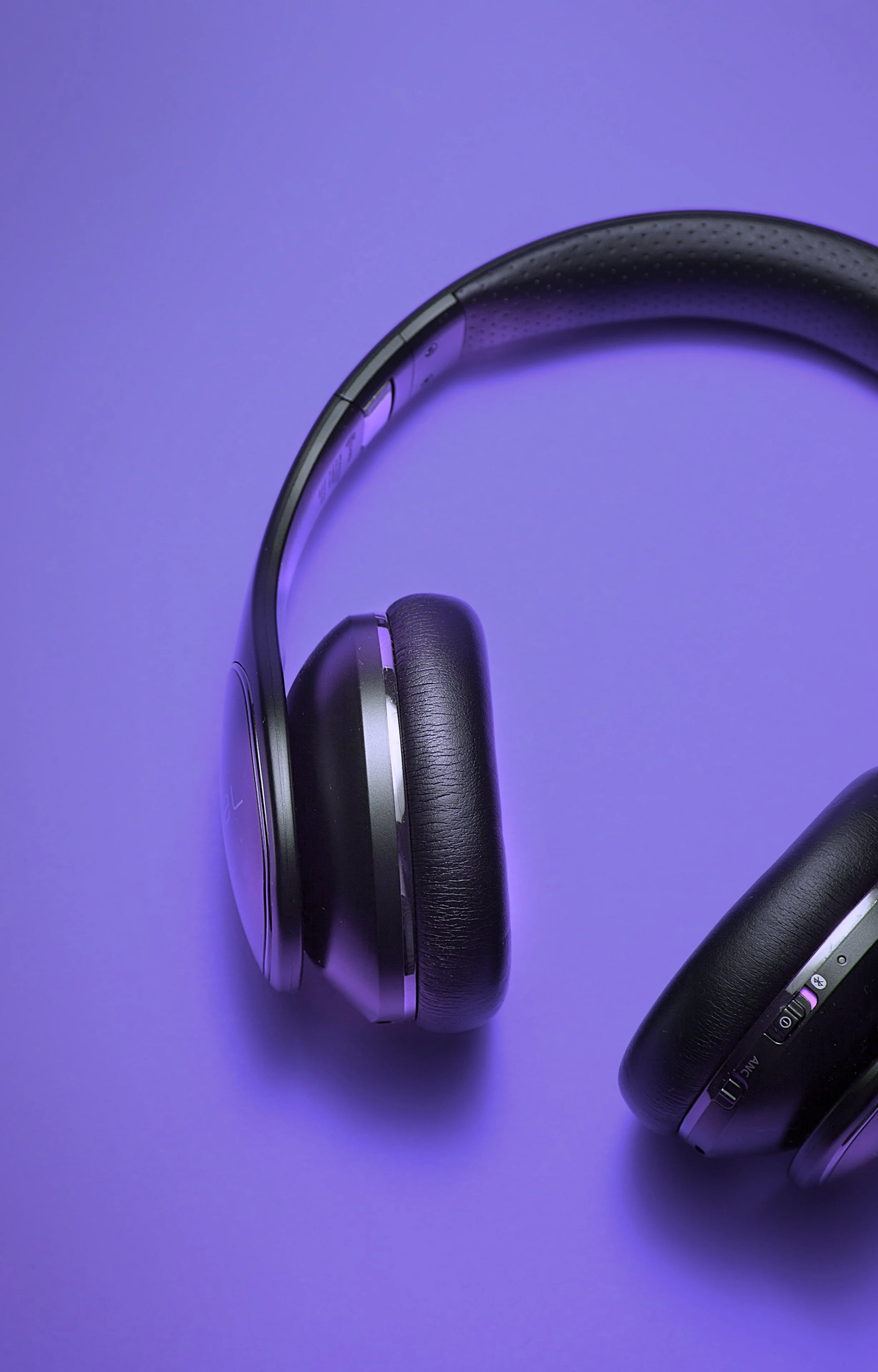 A pair of over-ear black headphones with silver accents resting against a purple background.