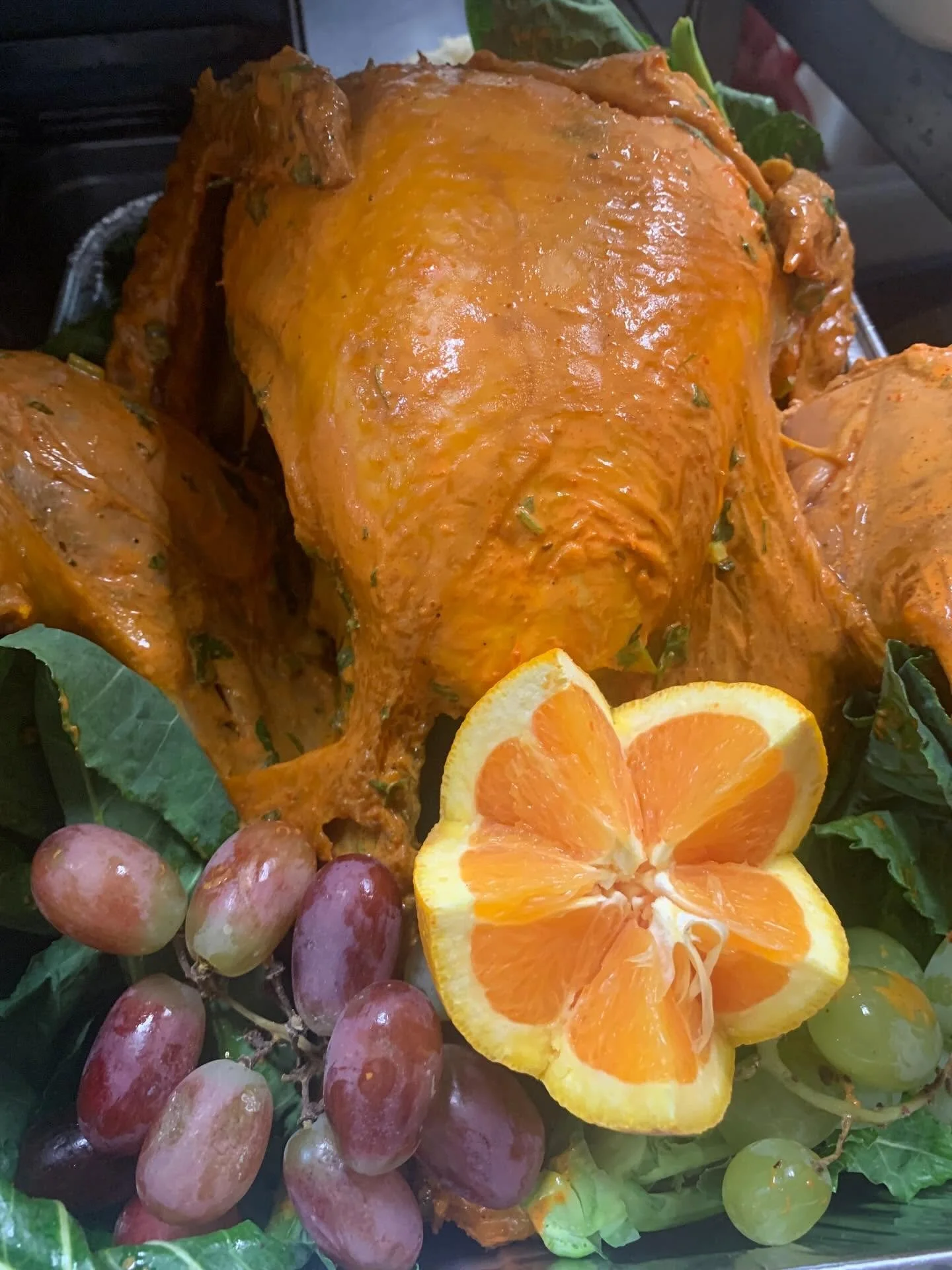 Baked chicken with orange sauce, surrounded by grapes, orange slices, and fresh green leaves.